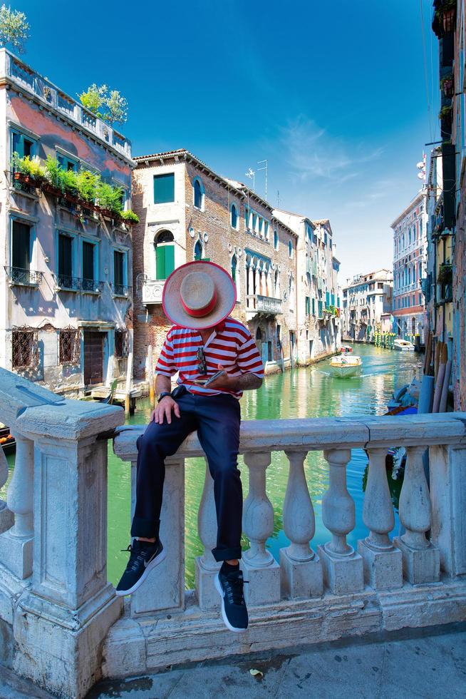 een Venetië gondelier zittend op een brug wacht op klanten foto