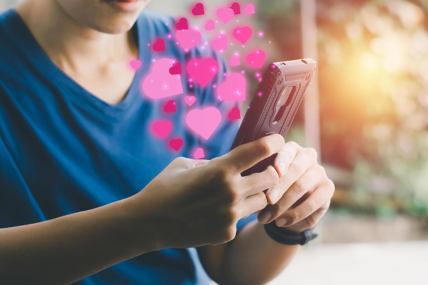 valentijn en nieuw normaal concept. hand met mobiel of smartphone en roze hartpictogram. sociale afstand voor je liefde. foto