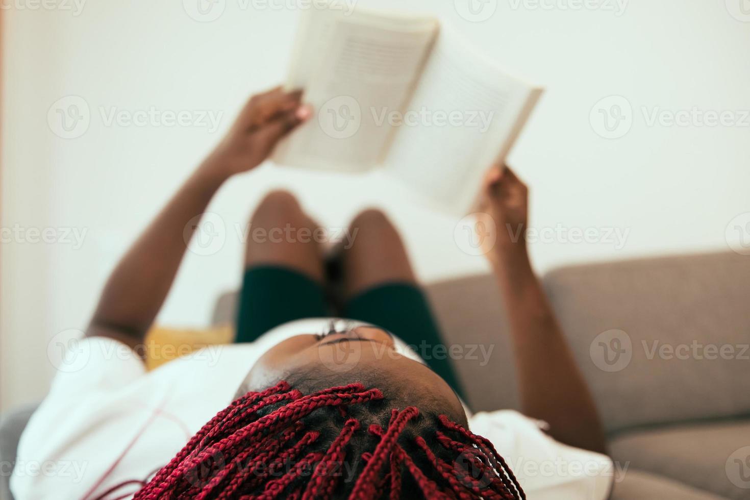 zwarte vrouw die op de bank ligt en een boek leest met zijn voeten op de muur foto