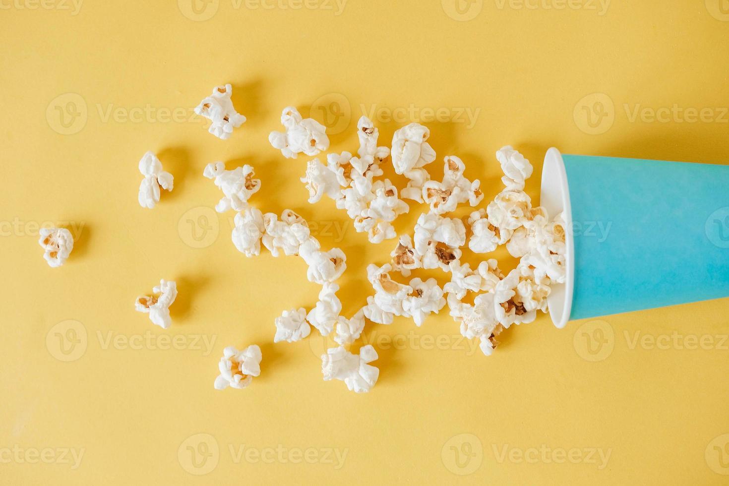 popcorn in een blauwe papieren beker verspreid over een gele achtergrond. minimalistisch concept. bovenaanzicht. kopiëren, lege ruimte voor tekst foto