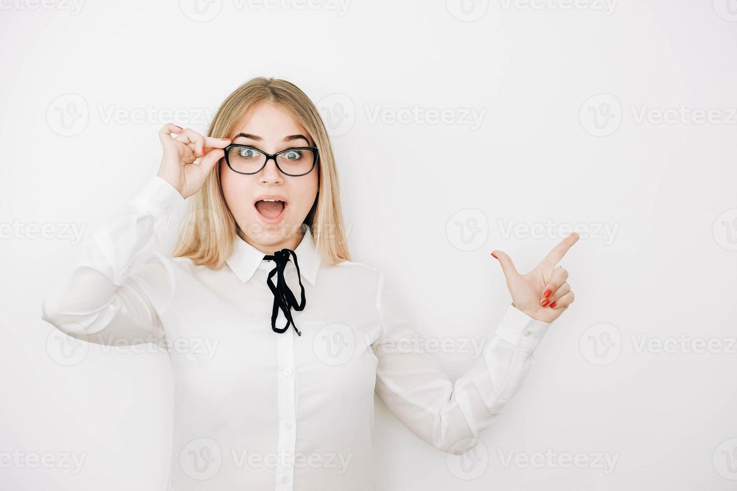 mooie jonge blonde vrouw met een stijlvol wit overhemd en een bril op een witte achtergrond verbaasd en verrast wijzend met de vinger naar de kopieerruimte. kopiëren, lege ruimte voor tekst foto