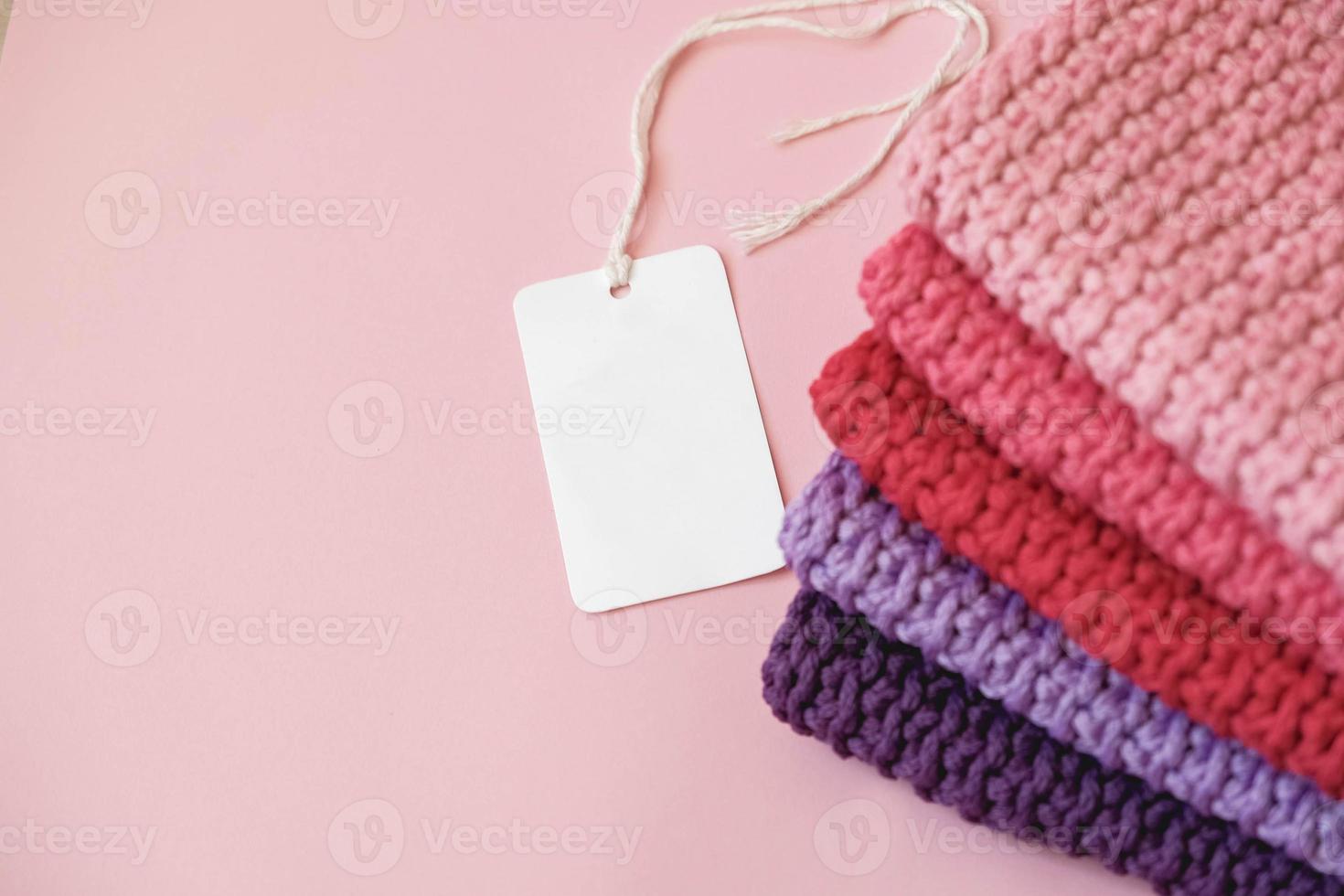stapel gebreid materiaal van draden van roze, rode, paarse kleuren met een leeg prijskaartje op een roze achtergrond. bovenaanzicht. kopiëren, lege ruimte voor tekst foto