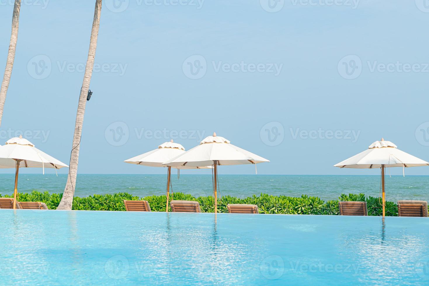 parasol met bed zwembad rond zwembad met oceaan zee achtergrond foto