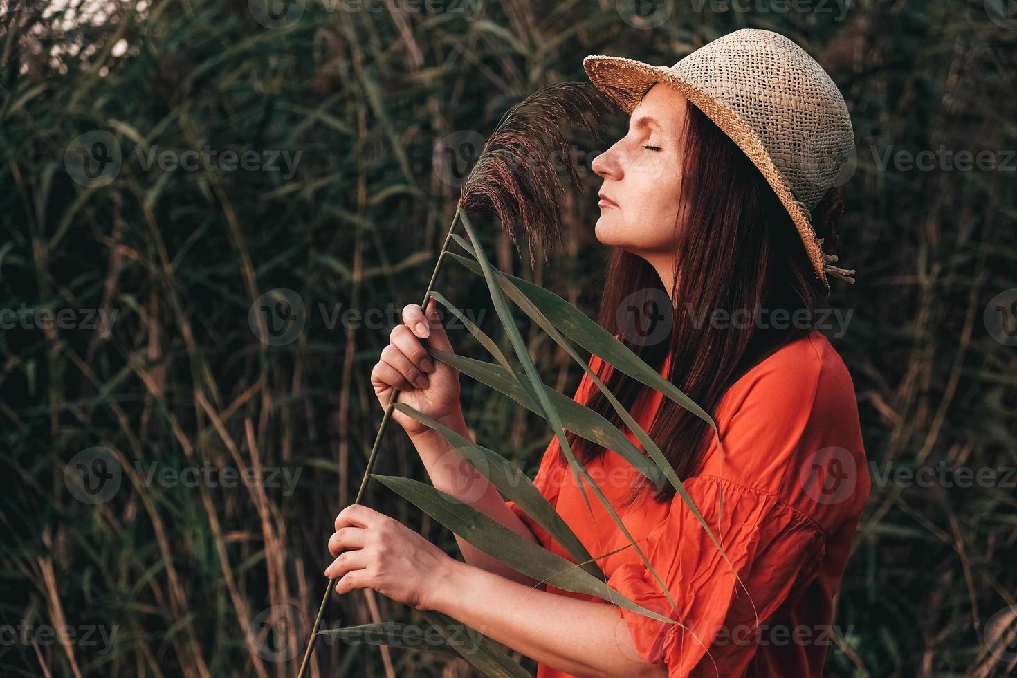 portret van een mooie vrouw in een strohoed en gekleed in rode kleren op een achtergrond van riet foto