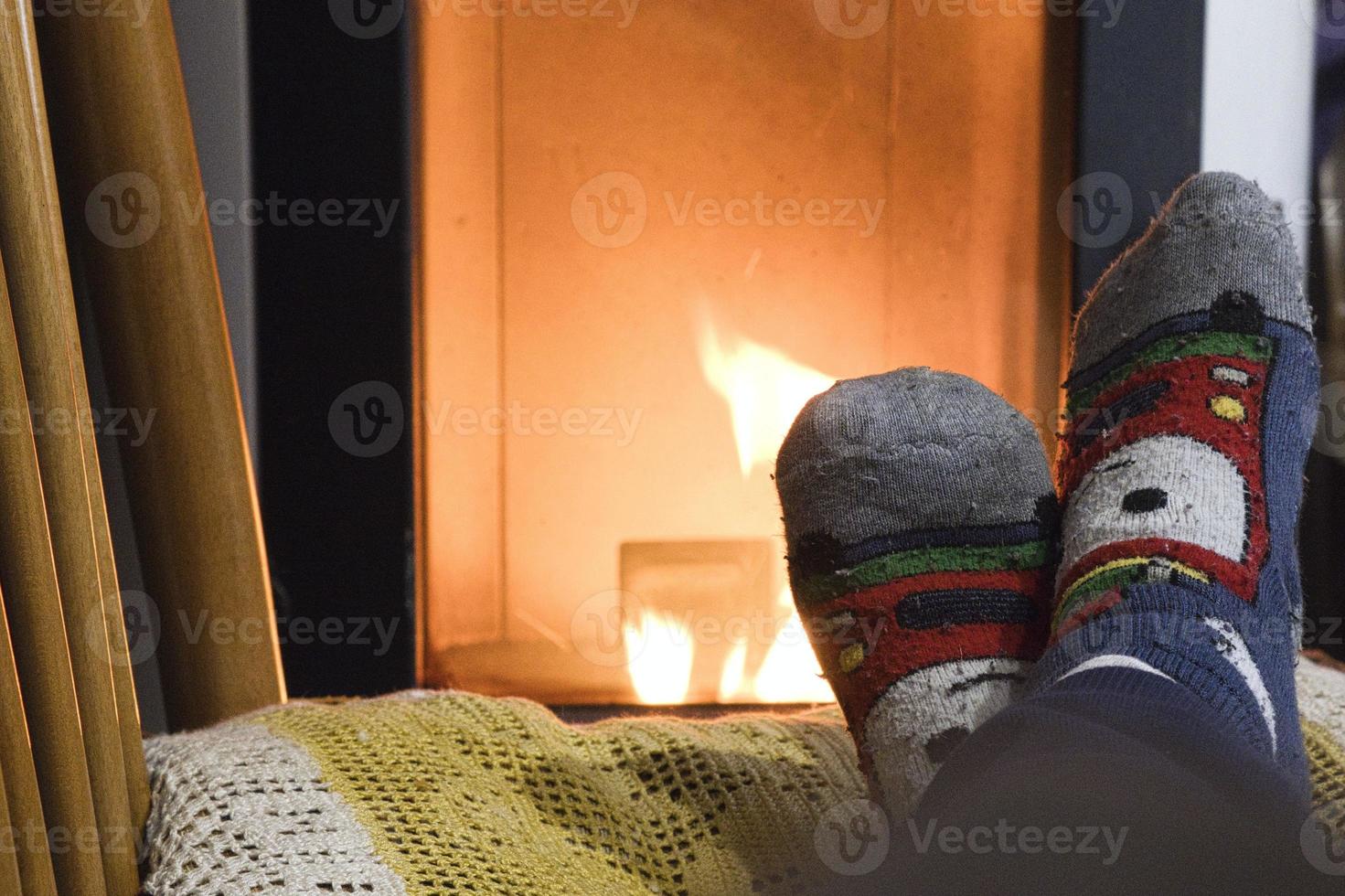 voeten opwarmen op een stoel voor een verlichte open haard tijdens een koude winteravond in december foto