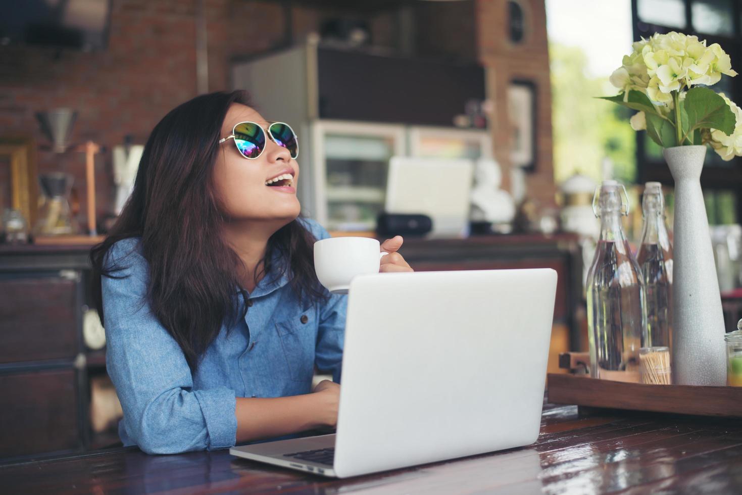 mooie jonge hipster vrouw zittend in een café met haar laptop, keek weg en glimlachte blij, ontspannend met vakantie, vrouw lifestyle concept. foto