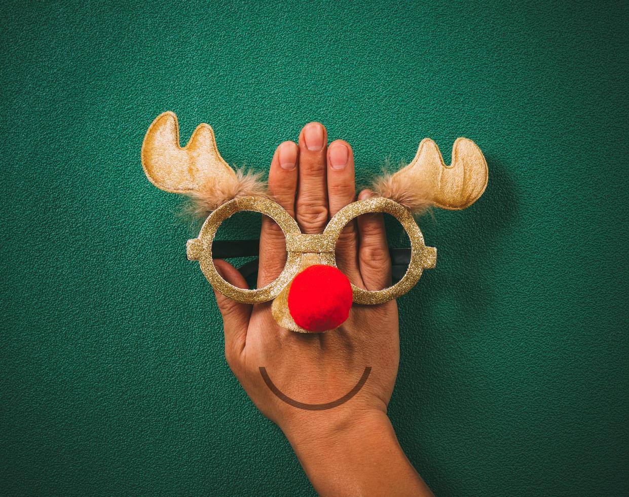 kerstbril die decoratie met kerstrendieren en rode bal bij de hand op groene achtergrond foto