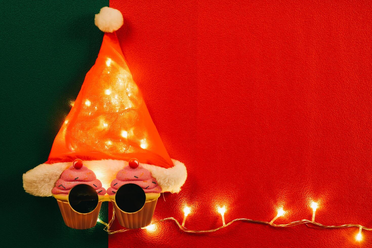 groet seizoen concept.santa claus hoed met ster licht en bril die decoratie met kerst cupcake op rode en groene achtergrond foto