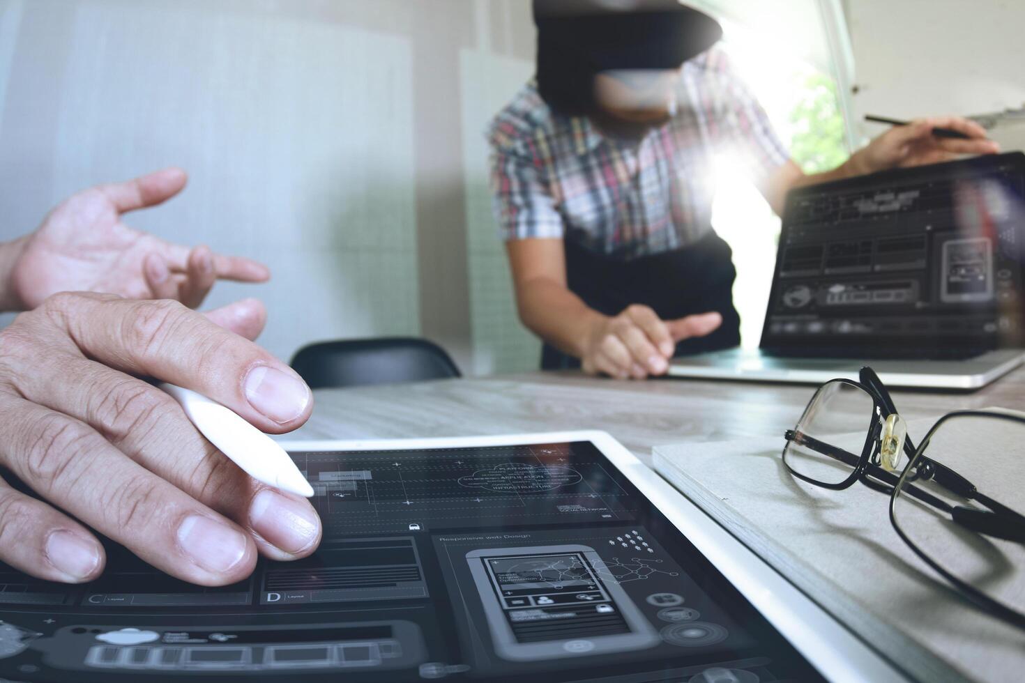 twee collega-swebontwerpers die gegevens en digitale tablet en computerlaptop bespreken met smartphone en ontwerpdiagram op houten bureau als concept foto