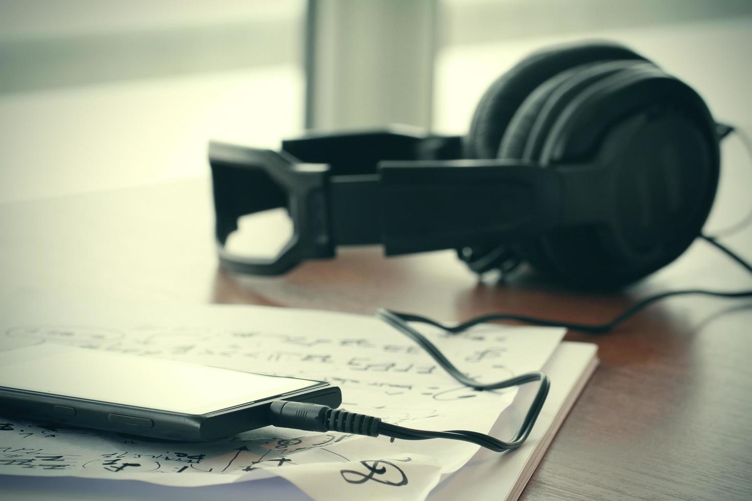 close-up jack van slimme telefoon met koptelefoon op muzieknoten papier met ondiepe dof gelijkmatig op houten bureau foto