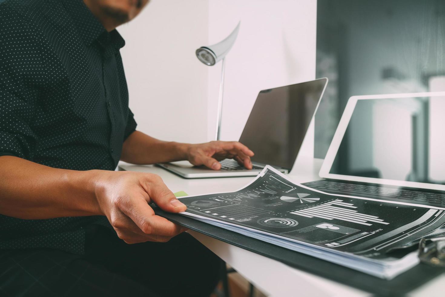 zakenman die met slimme telefoon en digitale tablet en laptop computer en document in modern bureau werkt foto