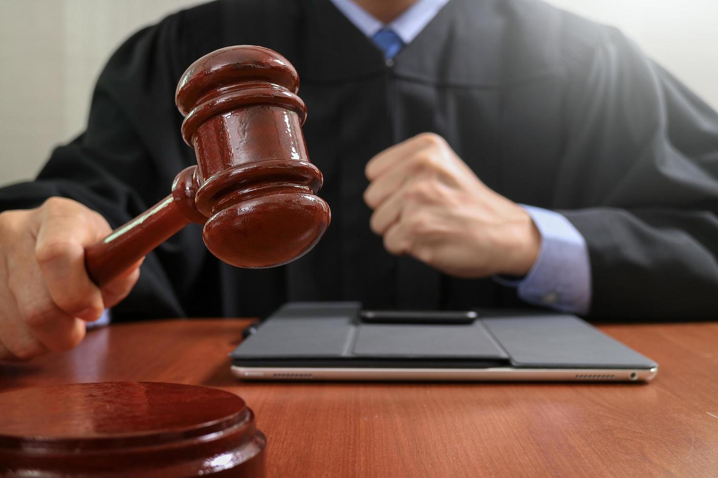 rechtvaardigheid en recht concept.male rechter in een rechtszaal die de hamer slaat, werkend met digitale tabletcomputer docking toetsenbord op houten tafel foto