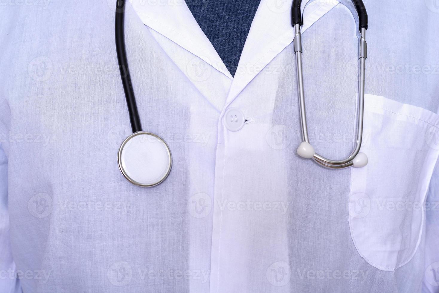 close-up van een mannelijke arts die een witte medische jas en een stethoscoop met een t-shirt draagt. foto