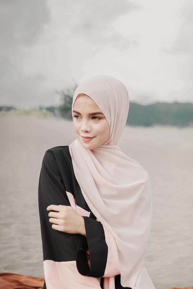 mooi islamitisch vrouwelijk model met hijab-mode, een moderne trouwjurk voor moslimvrouwen die in het zand en op het strand zitten. portret van een Aziatisch meisjesmodel dat hijab gebruikt en plezier heeft op het strand met bomen foto