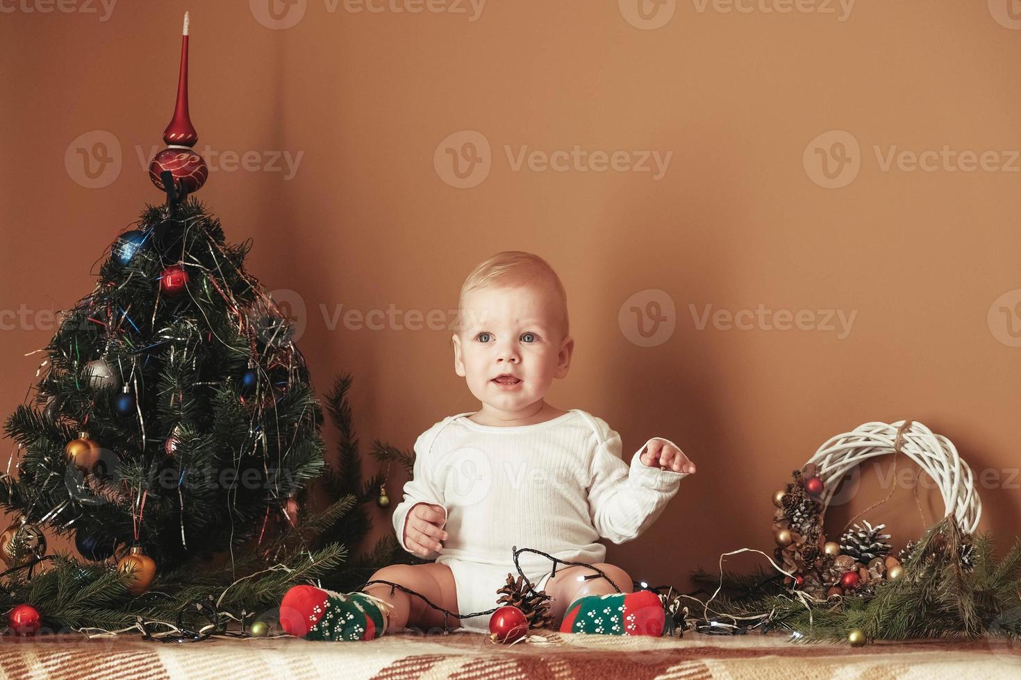 mooie kleine babyjongen die kerst viert. grappig kind in een kerstpak bij de kerstboom in de kamer foto