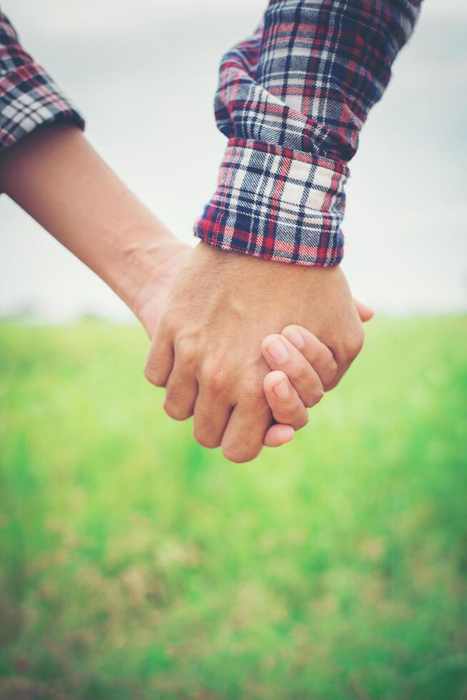 close-up van liefdevolle hipster paar hand in hand tijdens het wandelen op weiden veld. foto