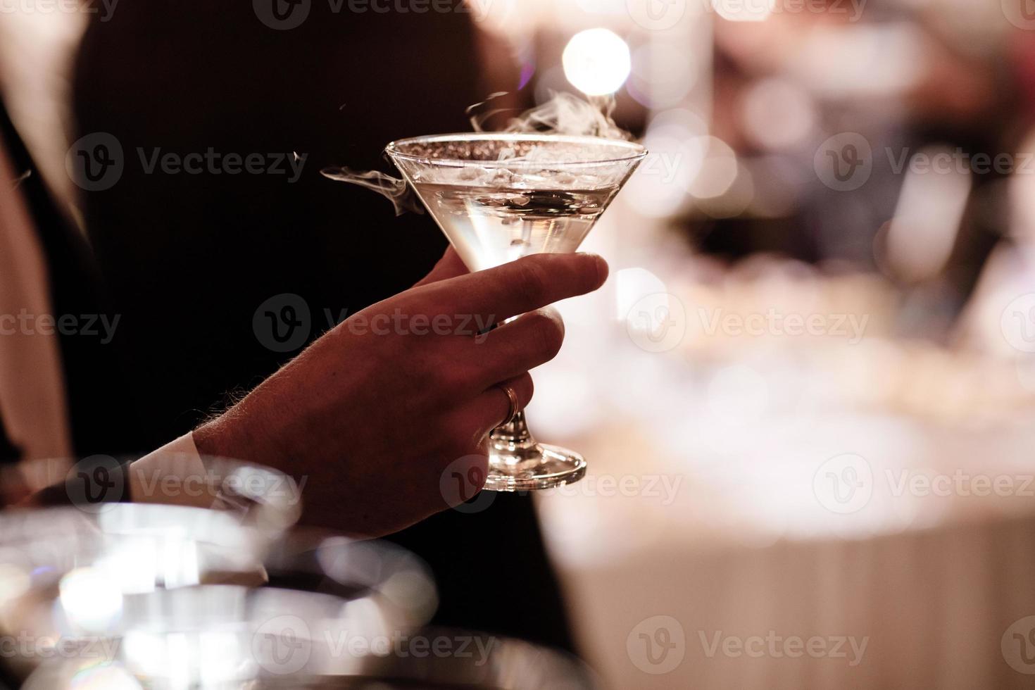 een close-up van de hand van een man die gekleed is in formele kleding en een martini-glas vasthoudt op een feestachtergrond. foto