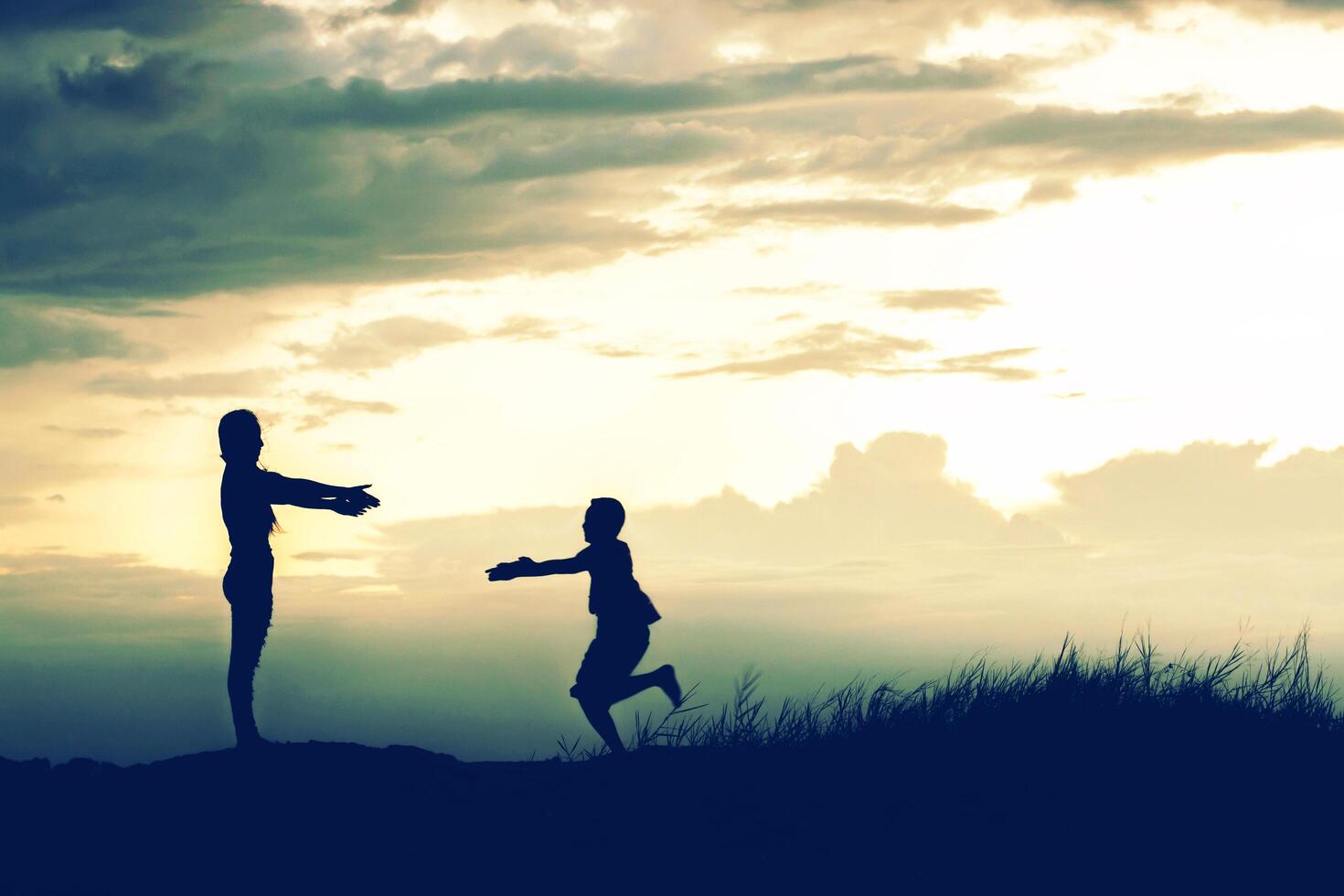 moeder moedigde haar zoon buiten aan bij zonsondergang, silhouetconcept foto