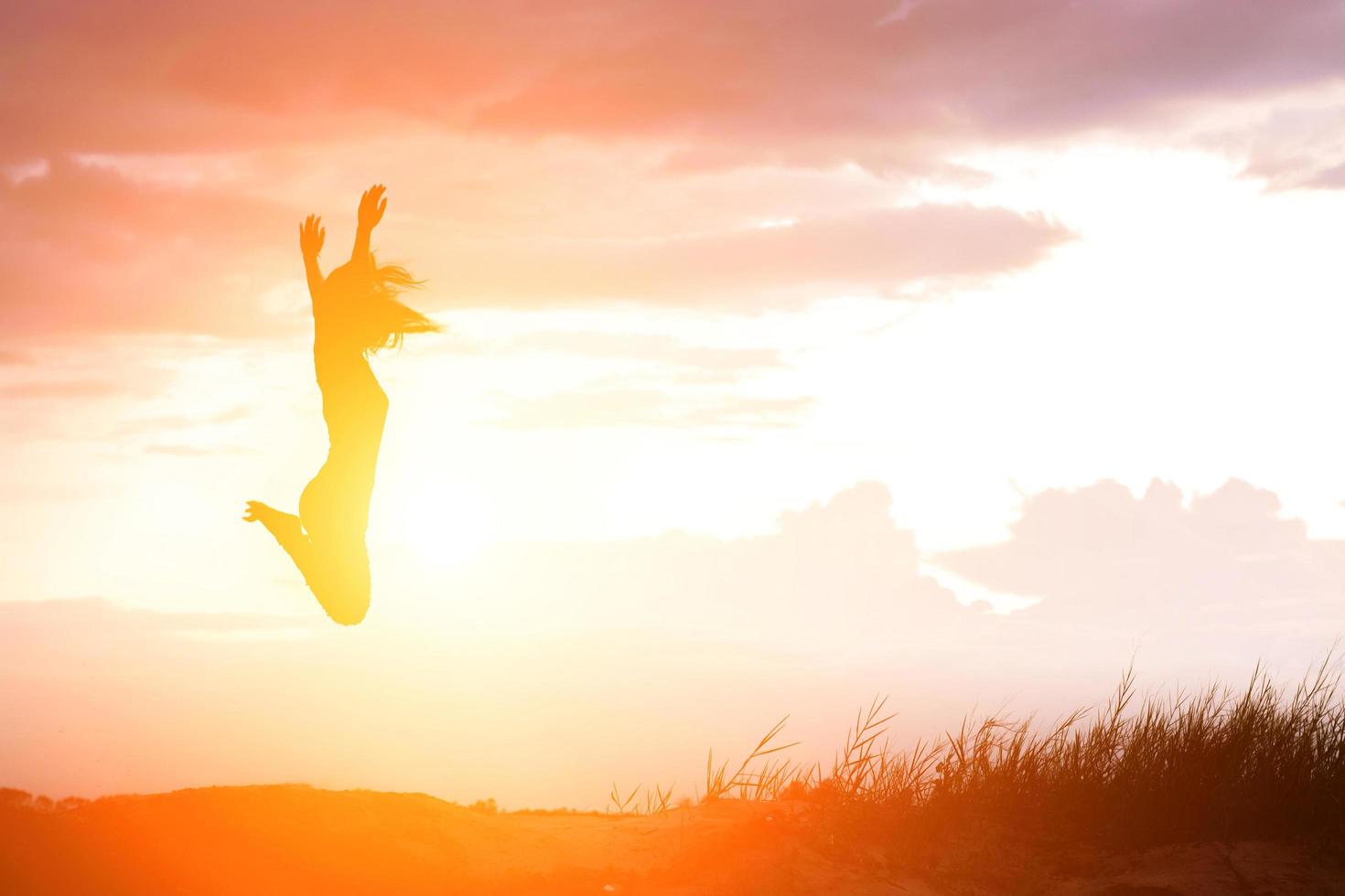 gelukkige vrouw die tegen mooie zonsondergang springt foto