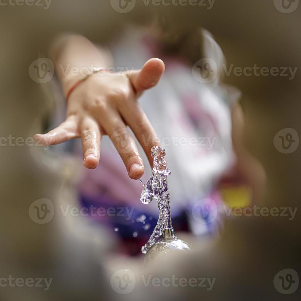 kinderhand spelen met drinkwater dat loopt van een oude waterpomp. foto