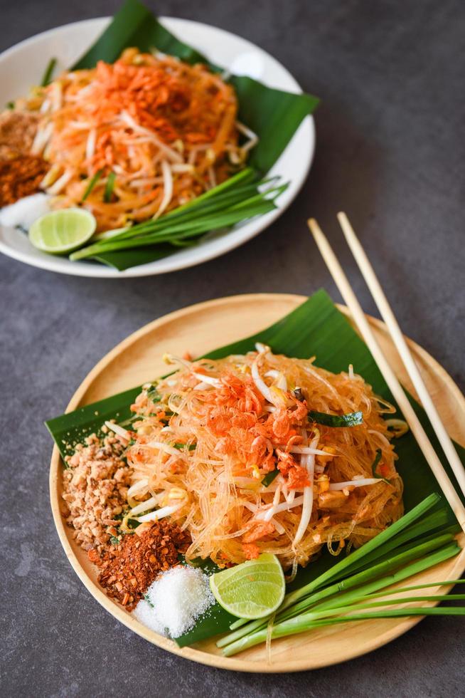 Thais eten gebakken noedels Thaise stijl met garnalen taugé en garnituur pinda's chili poeder suiker citroen limoen, roerbak noedels pad thai op bord geserveerd op de eettafel eten - bovenaanzicht foto