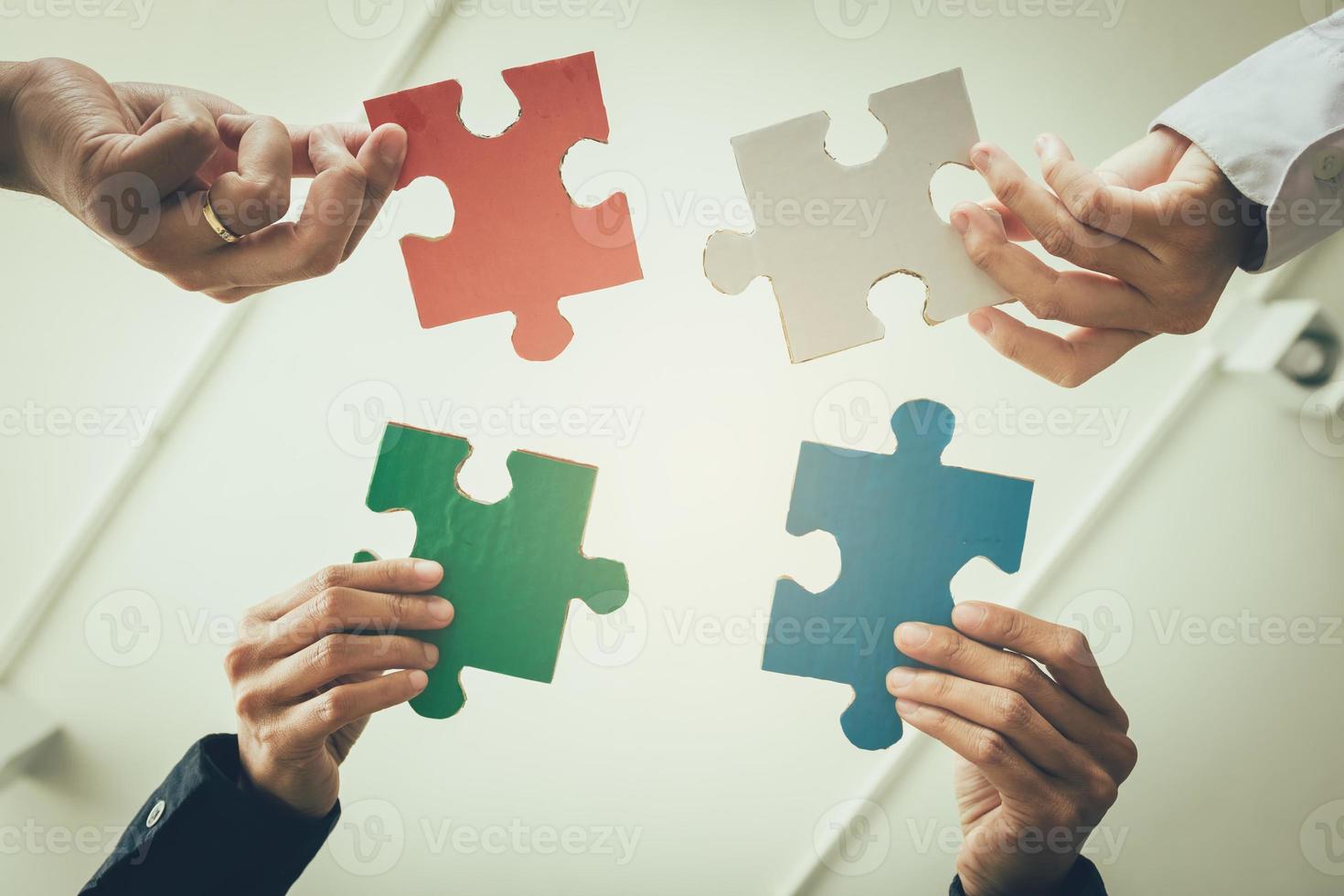 multi-etnische groep zakelijke professionals die vier puzzelstukjes in elkaar zetten. foto