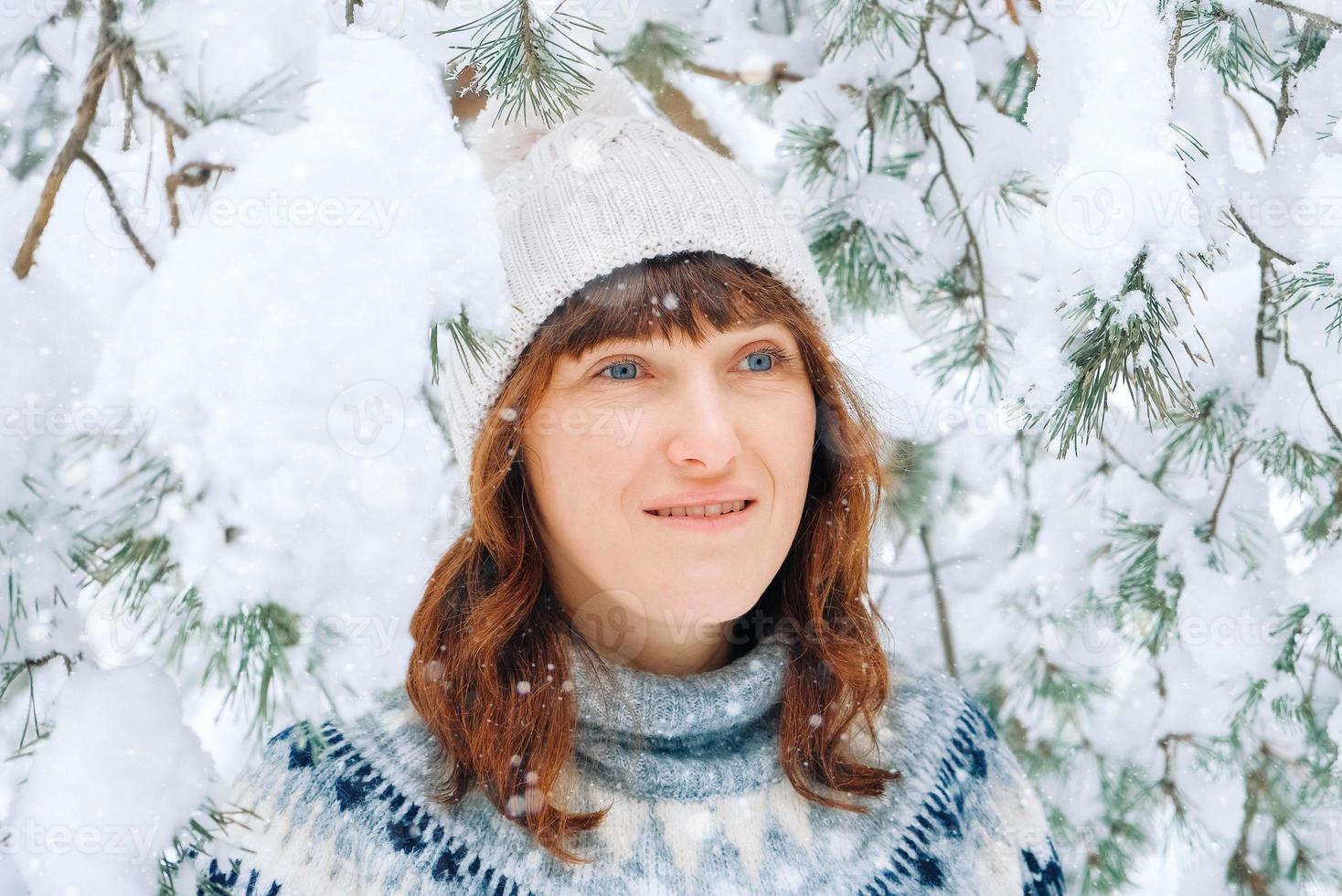 winterportret van een vrouw in een warme muts en trui op een achtergrond van besneeuwd bos foto