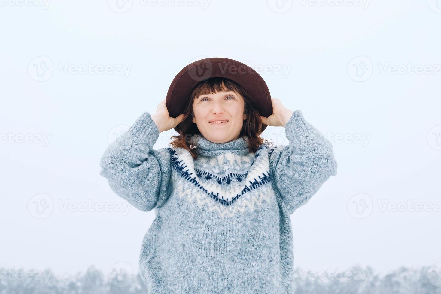 vrouw in een bruine hoed en trui op een achtergrond van besneeuwd bos foto