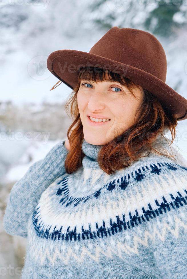 portret van een lachende vrouw in een bruine hoed en trui op een achtergrond van winterlandschap foto