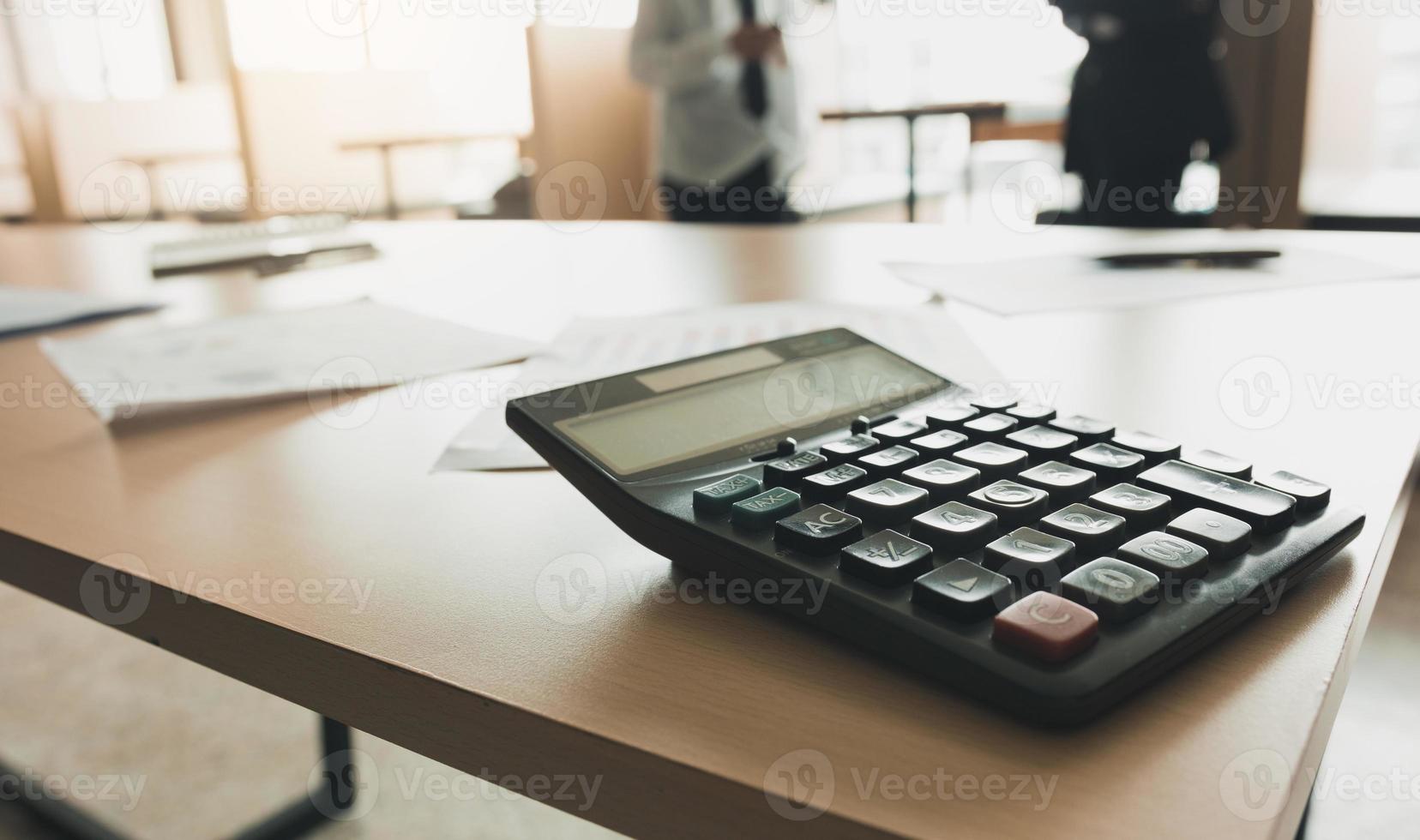 close up van rekenmachine op bureau met mensen uit het bedrijfsleven praten achtergrond. foto