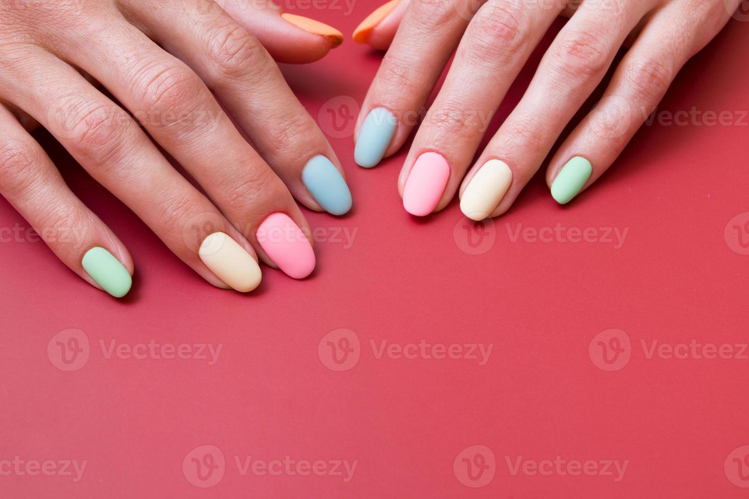 gekleurde matte manicure op vrouwelijke handen op rode achtergrond met kopieerruimte foto