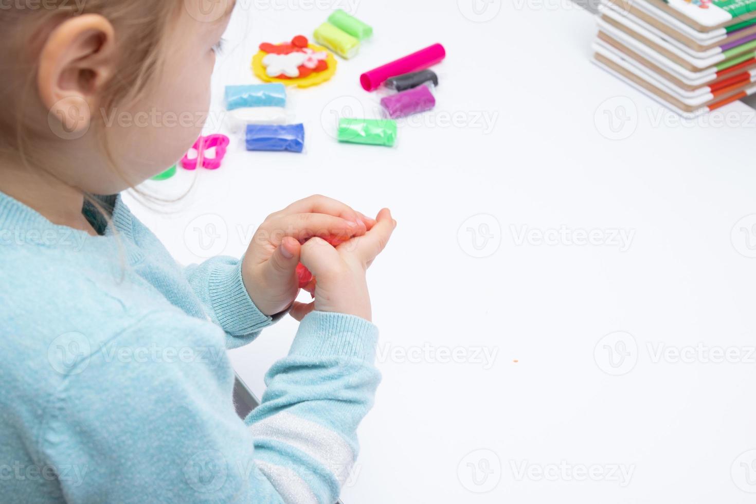 het meisje aan tafel speelt met boetseerdeeg. kinderspelletjes voor fijne motoriek foto