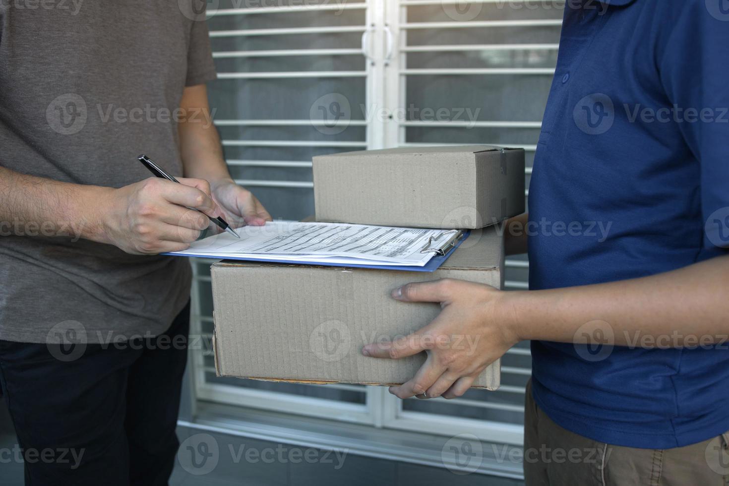 levering jonge man die aan de deur van huis staat en pakjes draagt voor een jonge man om te ondertekenen. foto