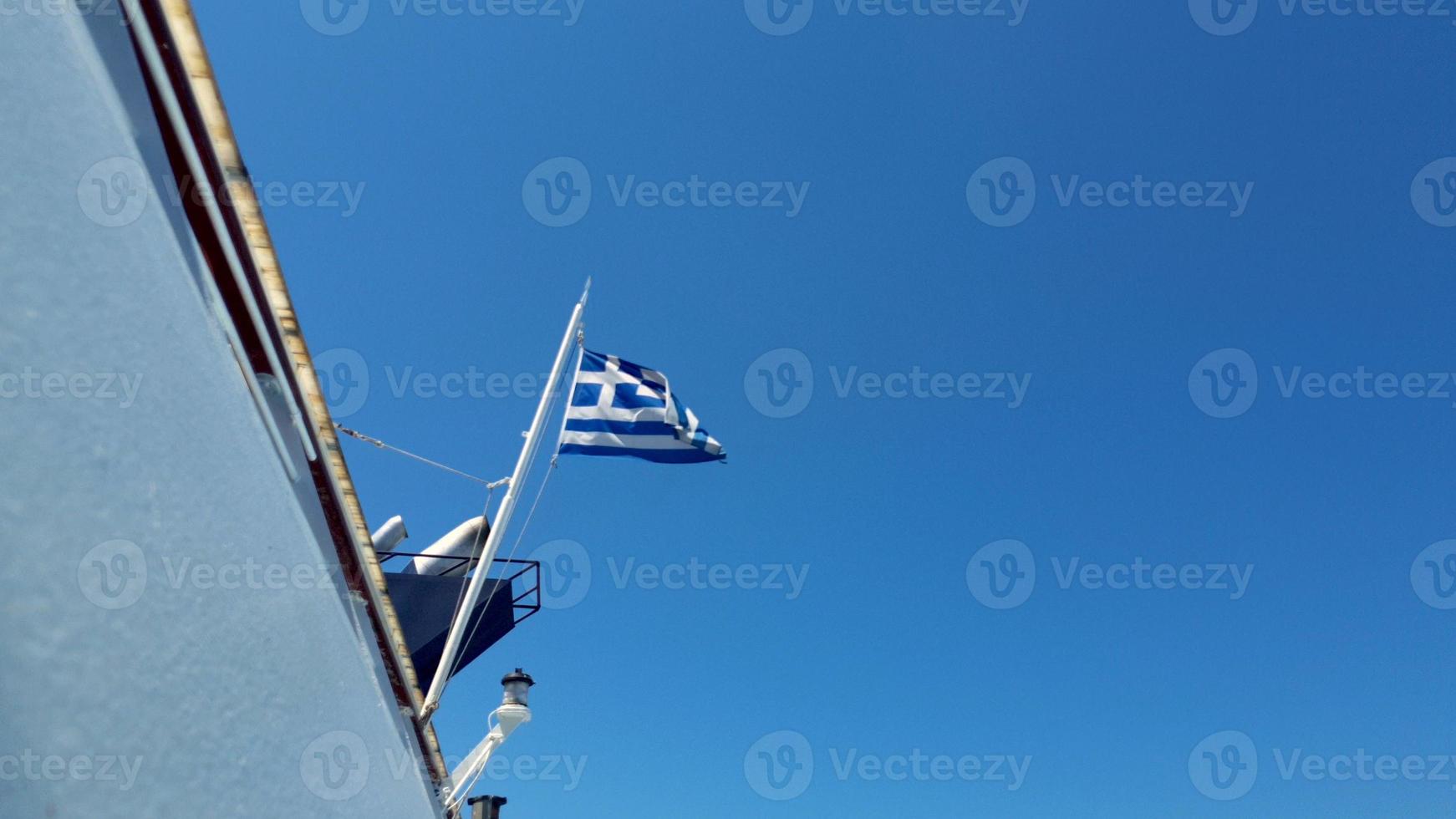 griekse vlag zwaaien in de achterkant van een veerboot in de egeïsche zee tegen een bewolkte hemel. foto