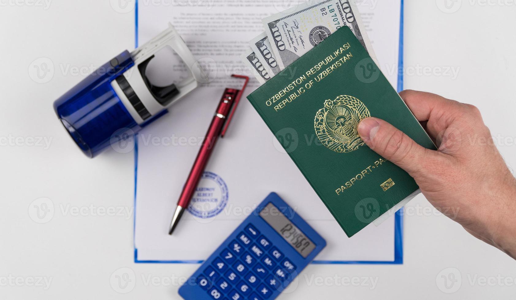 hand houdt het paspoort van oezbekistan met Amerikaanse dollars op de achtergrond van documenten en rubberen stempel. concept - omkoping en corruptie foto