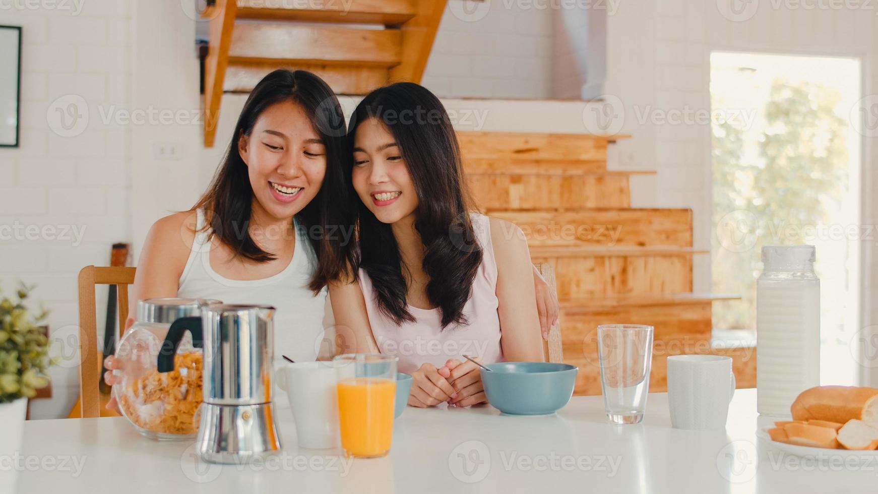 Aziatische lesbische lgbtq-vrouwen hebben thuis ontbijt, jonge Aziatische minnaar die zich gelukkig voelt, drinkt sap, cornflakes, granen en melk in kom op tafel in de keuken in de ochtendconcept. foto