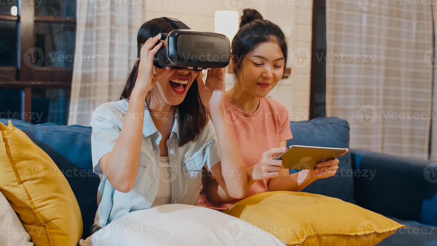 lesbische lgbt-vrouwen koppelen thuis tablet, aziatische vrouw voelt zich gelukkig met laptop en vr die samen games spelen terwijl ze 's nachts op de bank in de woonkamer liggen. minnaar viert vakantieconcept. foto