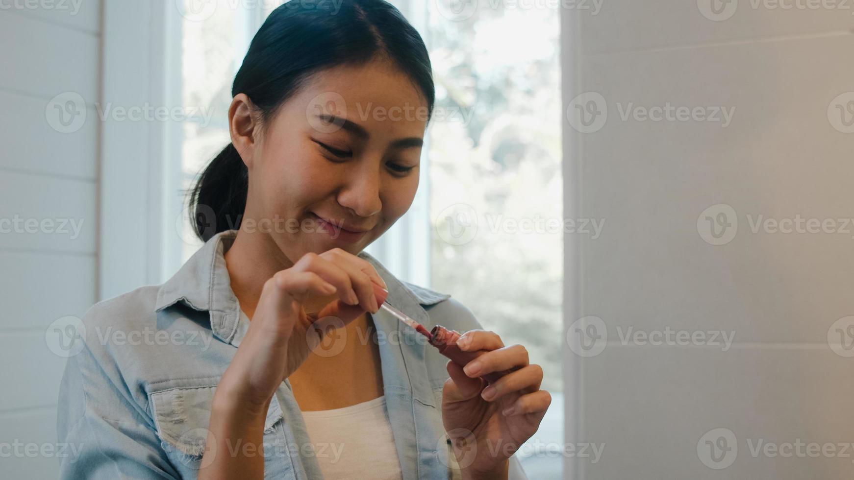 mooie aziatische vrouw die lippenstift make-up voor de spiegel gebruikt, gelukkige chinese vrouw die schoonheidscosmetica gebruikt om zichzelf te verbeteren, klaar om thuis in de badkamer te werken. lifestyle vrouwen ontspannen thuis concept foto