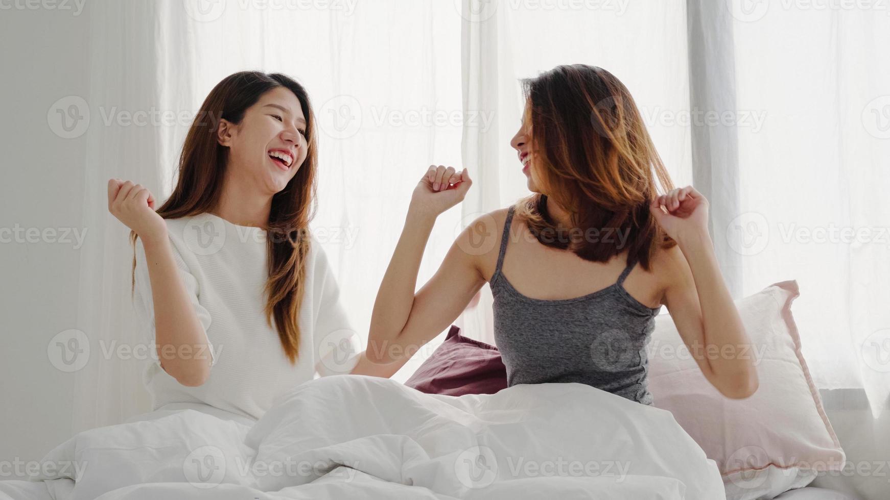 mooie jonge aziatische vrouwen lgbt lesbische gelukkige paar of meisjes vrienden dansen op streaming muziek met wild plezier in pyjama's op bed in tiener slaapkamer rondhangen thuis. leuke tijd thuis doorbrengen. foto