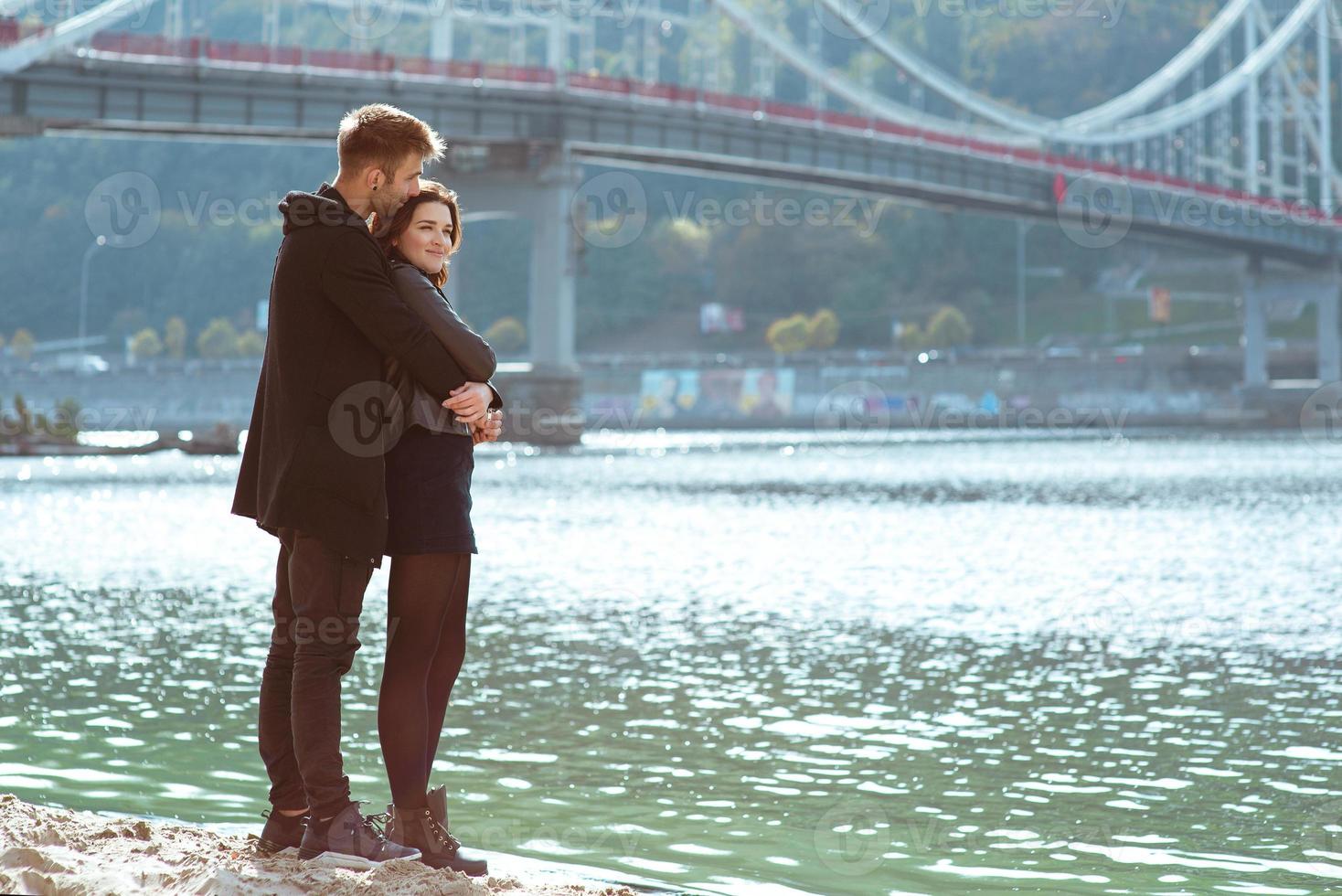 mooie geweldige grappige vrolijke jonge paar knuffelen buiten bij de rivier op de achtergrond van de brug. vriendinnetje en vriendje. familie, liefde en vriendschap concept foto