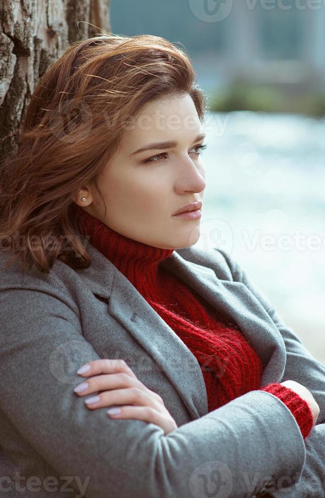 jonge mooie brunette depressieve trieste vrouw bij de rivier in de stad op de achtergrond van de brug foto