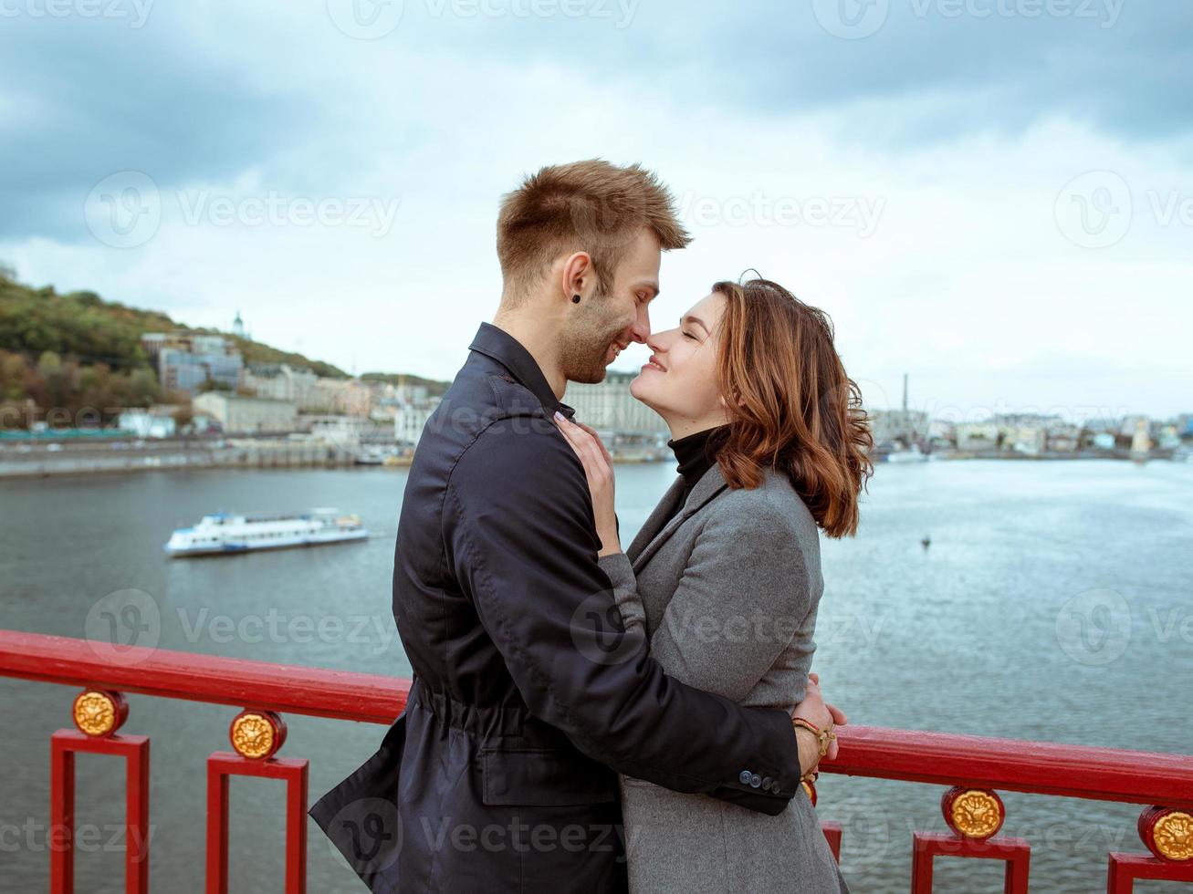 mooie geweldige grappige vrolijke jonge paar knuffelen buiten bij de rivier op de achtergrond van de brug. vriendinnetje en vriendje. familie, liefde en vriendschap concept foto