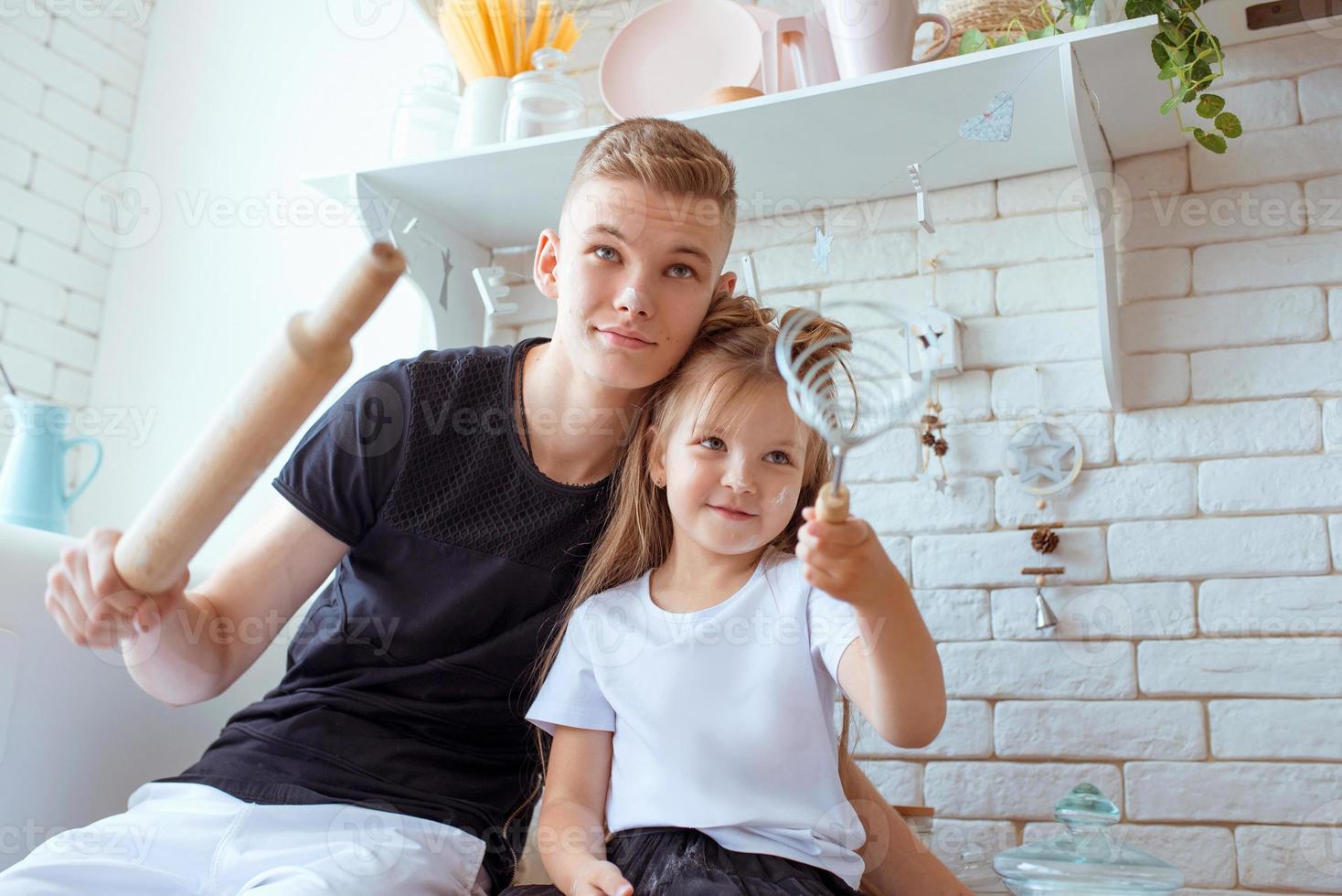 Kaukasische grappige schattige broers en zussen in de keuken - klein meisje met oudere broer bakken in de keuken. bak en culinair concept foto