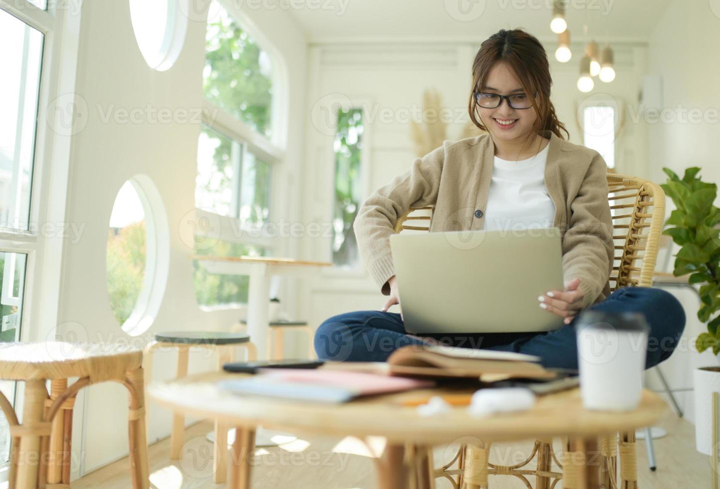 een jonge vrouw zit thuis in de woonkamer met een laptop die online praat. foto