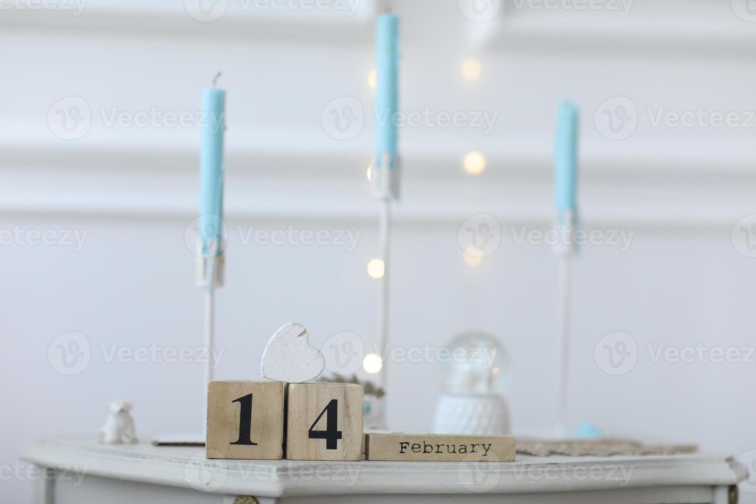 Valentijnsdag concept. datum 14 februari op houten kubuskalender op een witte geschenkdoos en een wit hart in de hand. bokeh gouden en witte achtergrond foto