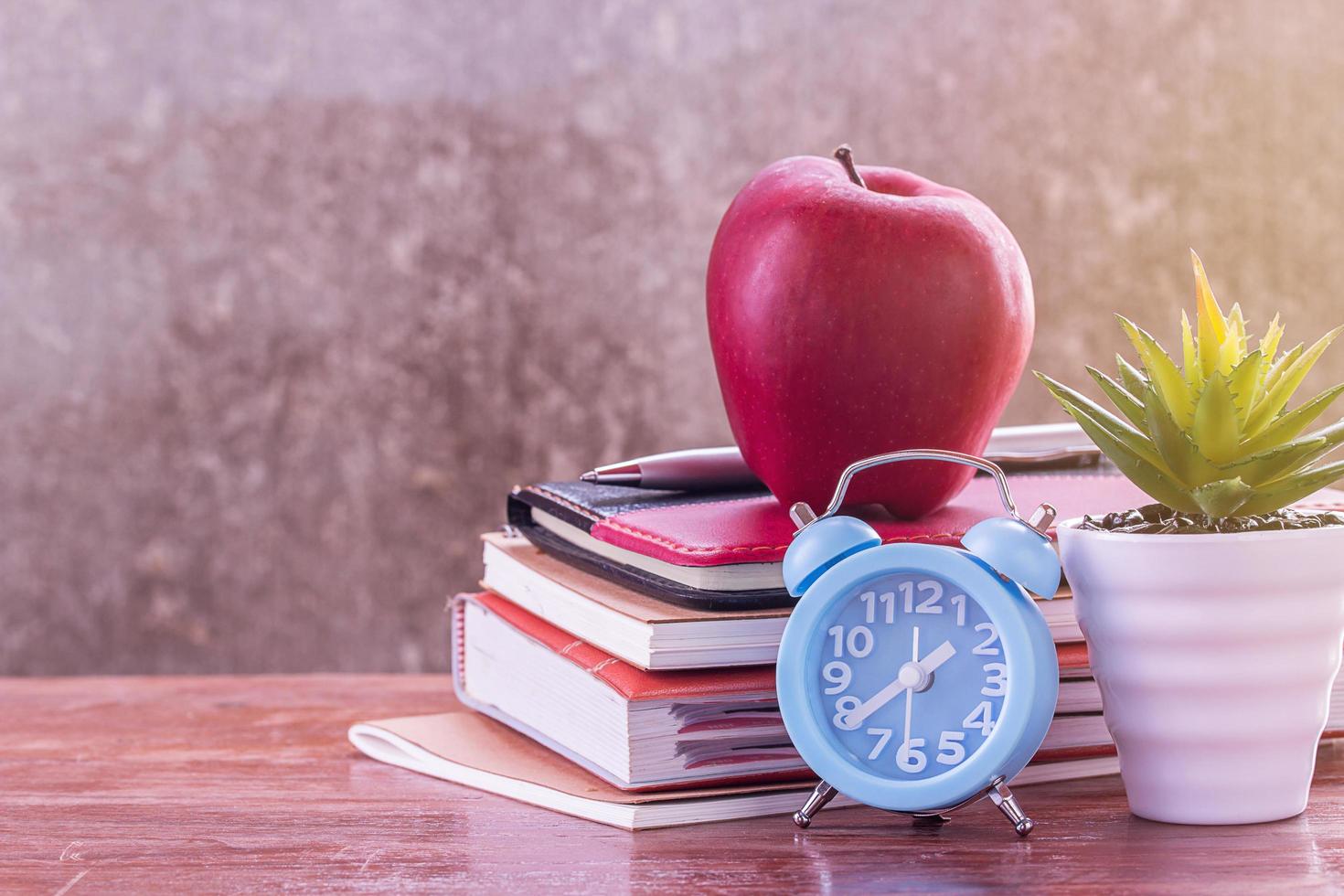 terug naar school, notebook, wekker, rode appel, bloem op houten tafel met onscherpe achtergrond foto