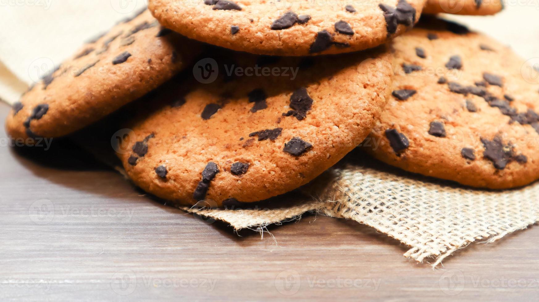 Amerikaanse chocoladeschilferkoekjes op een bruine houten tafel en op een close-up van een linnen servet. traditioneel afgerond knapperig deeg met chocoladeschilfers. bakkerij. heerlijk dessert, gebak. landelijke stilleven. foto