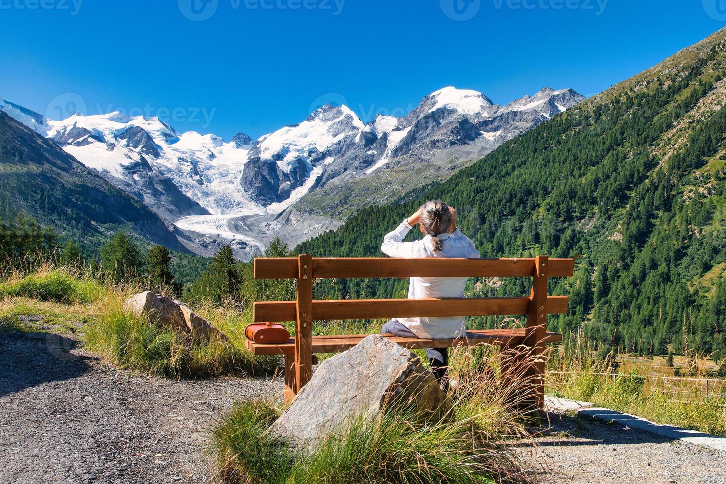 een oudere toerist observeert de bergen vanaf een bankje foto