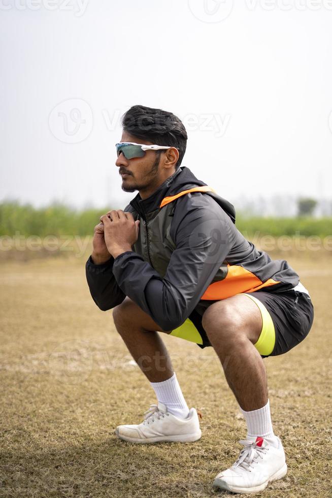 sport en gezond leven concept - Indiase jonge sportman met fitnesskleding die squats doet en traint op een veld. foto