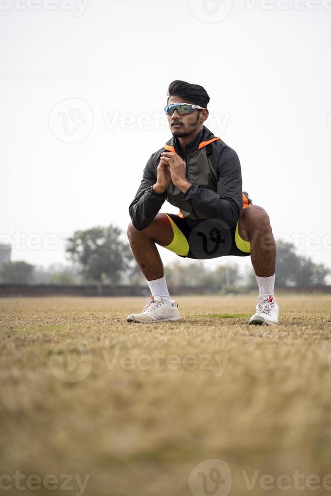 jonge Indiase sportman doet squats in het veld. sport en gezonde levensstijl concept. foto